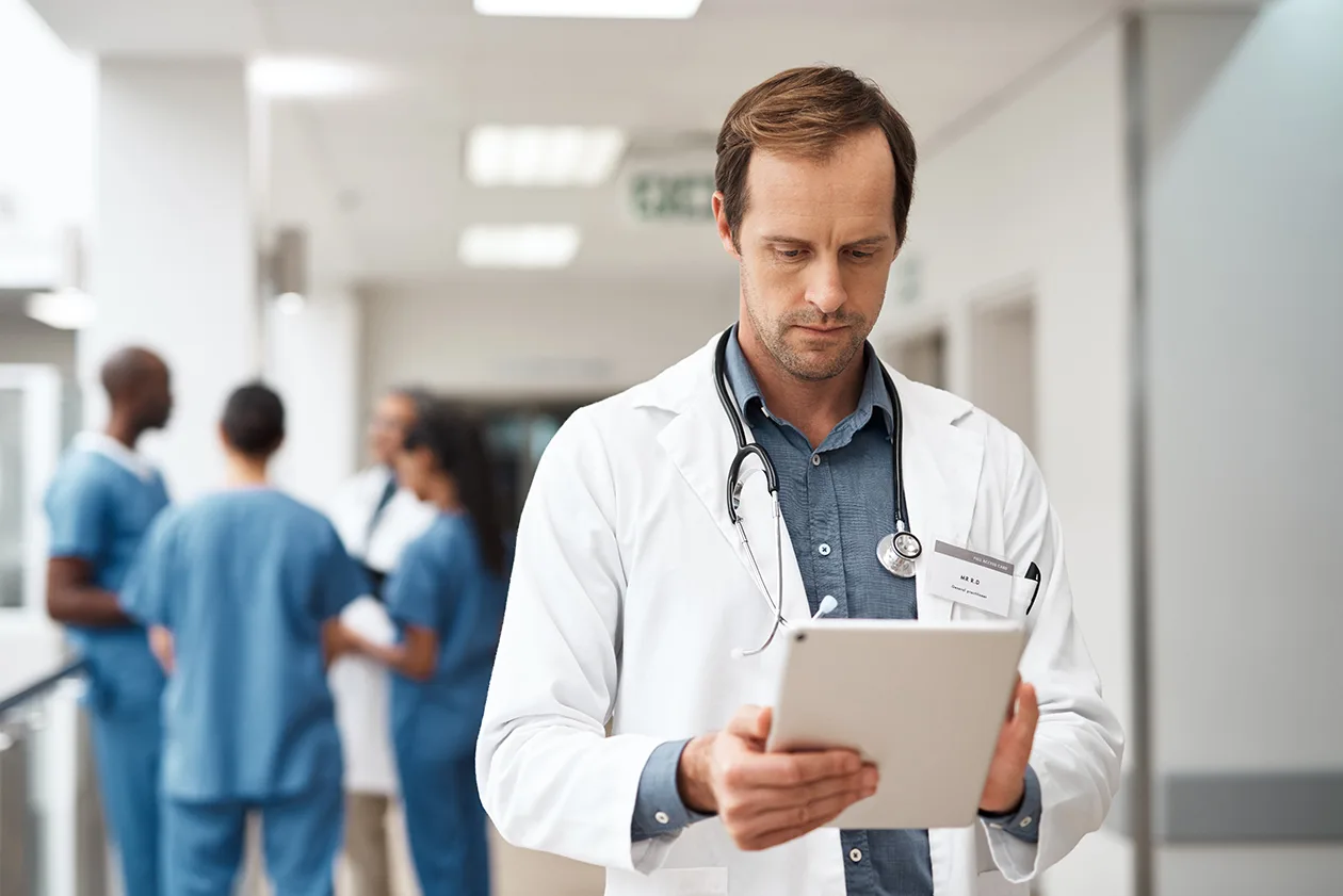 Male doctor in white coat working on a tablet in a hospital hallway