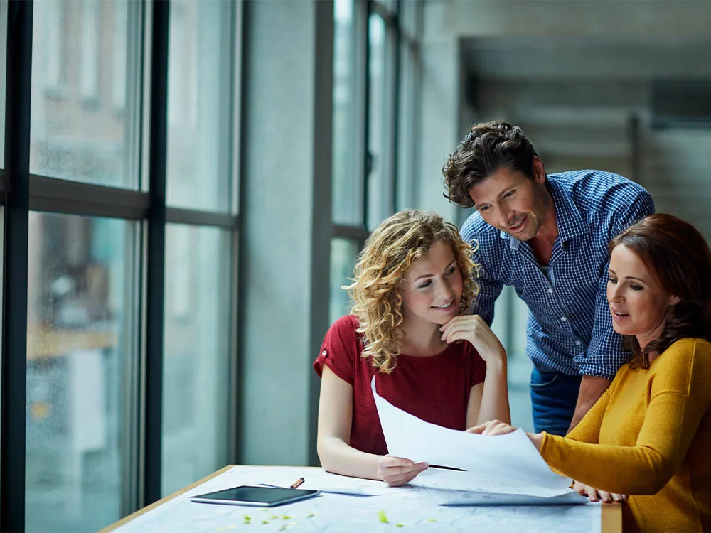 Three people standing around a table looking at a piece of paper