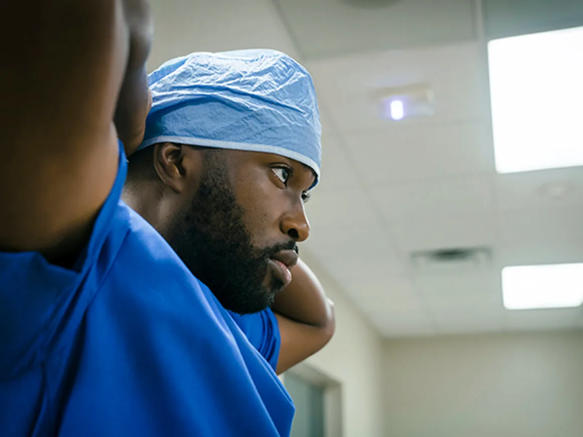 Male doctor in blue scrubs secures his scrub cap